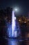 Colored luminous fountain in the middle of the lake at night with full moon.