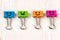Colored metal binder clips of blue, green, pink and orange color smiles on white wooden background with copy space