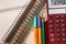 Colored pencils, desktop calculator and notebooks on white wooden table.  School and office supplies. Top view