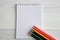 Colored pencils lie on an open notebook in a ruler on a white wooden table. Black, green, blue, orange and pink pencils lie on a