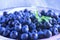 A colored photo of blueberries with green leaves on the plate. Fresh ripe juicy bilberries, bright autumn colorful background. Con