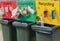 Colored public recycling signs with examples attached to waste bins