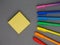 Colored scattered bright rainbow pens and yellow square sticky post it paper sheets laying on grey background