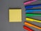 Colored scattered bright rainbow pens and yellow square sticky post it paper sheets laying on grey background