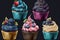 A colorful assortment of cupcakes with swirled cream frosting and berries including vanilla, chocolate, blueberry, and raspberry.