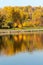 Colorful autumn. Alley along the riverbank on the background of the autumn park. Reflections in the river