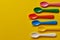 Colorful baby plastic spoons on yellow background. Many, utensils. Top view.
