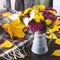 A colorful bouquet of chrysanthemum flowers in a vintage vase, pumpkins, yellow autumn leaves, a woolen scarf.