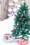 Colorful boxes of gifts on snow and artificial fir tree decorated with Christmas red toys outdoors in yard in snowy background
