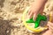 Colorful and bright plastic yellow bucket and green star in child`s hands on background of sea sand / child`s play with sand