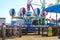 Colorful carnival rides with people riding and people standing around the rides surrounded by lush green palm trees