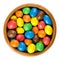 Colorful chocolate peanut candies in wooden bowl over white