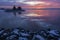 Colorful cloudy sunset sky reflected in the sea with snowy stones on the shore