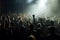 Colorful concert crowd in front of a lit stage inside a concert venue, during a music festival