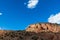 A colorful desert mesa with sandstone rock formations and cliffs under a vast blue sky illuminated by sunlight through breaks in