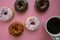 Colorful donuts on a pink table being served for breakfast with piping hot coffee.