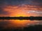 Colorful and dramatic sunset sky reflecting on pond water. Silent evening scene at Delia lake. Vibrant sundown clouds at the