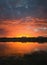 Colorful and dramatic sunset sky reflecting on pond water. Silent evening scene at Delia lake. Vibrant sundown clouds at the