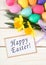 Colorful Easter Eggs and Daffodil Flowers still life on Rustic White Board Background with Happy Easter in words or text on greeti