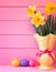 Colorful Easter Eggs in Nest with Daffodils in Vase on Pink Boards Background with room or space for copy, text, or your words.