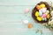 Colorful Easter eggs in nest with flower on rustic wooden planks background in blue paint. Holiday in spring season