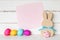 Colorful Easter Eggs with Pink Paper Invite Card and a Simple Bunny and Chick against White Shiplap Board Background wall