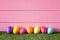 Colorful Easter Eggs in Row on Bottom of Pink Wood Boards Wall Background and Laying in Green Grass with room or space for copy