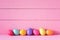Colorful Easter Eggs in a Row on a Table and against a Bright Pink Board Wall Background with copy space. Horizontal and wide with