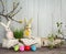 Colorful eggs, funny handmade textile Easter bunnies and spring branches with leaves and flowers on a light wooden background.