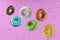 Colorful flying doughnuts with sprinkles on pink background.
