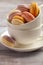 Colorful French macaroons in white cup on wooden background