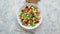 Colorful fresh vegetable salad with feta cheese in a white deep bowl closeup on a stone table