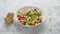 Colorful fresh vegetable salad with feta cheese in a white deep bowl closeup on a stone table