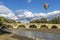 A colorful hot air balloon flies over the ancient Buriano Bridge, Arezzo, Italy