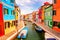 Colorful houses in Burano near Venice, Italy with boats, canal and tourists. Famous tourist attraction in Venice