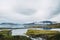 Colorful Icelandic landscapes under gray heavy sky. Green wet grass, beautiful lake, and snowy tops of the mountais reflected in