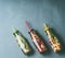 Colorful infused water in bottles with fruits berries, cucumber, herbs and drink straws on gray background, top view. Tasty summer