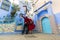Colorful journey from Morocco. Young couple in red dress walking in the medina of the blue city Chefchaouen