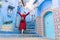 Colorful journey from Morocco. young tourist in red dress walking in the medina of the blue city Chefchaouen