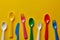 Colorful kids plastic spoons on yellow background. Many, utensils.