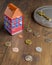 A colorful little house shaped piggy bank on a wooden table with coins and a safe key
