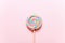 Colorful lollipop swirl on stick. Striped spiral multicolored candy on pink background, top view