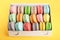 Colorful macarons in box on yellow white background closeup