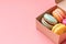 colorful macarons in the cardboard box on the pink background