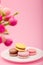 Colorful macaroons on white plate on pink background, flowers. Mothers women Valentines day, birthday, spring Easter