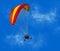 A colorful motorized paraglider flies against a blue sky. Sunny background with people paragliding.