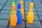 Colorful orange, blue, green and yellow plastic bowling game on dark grey surface in a park in a summer day