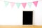 Colorful party flags hanging over blank white vintage wooden frame on wood table background, birthday, anniversary, celebrate eve