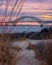 Colorful pastel dusk sky behind a long steel tied arch bridge. Fire Island Inlet Bridge