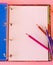 Colorful pencils on the journal on a pink surface